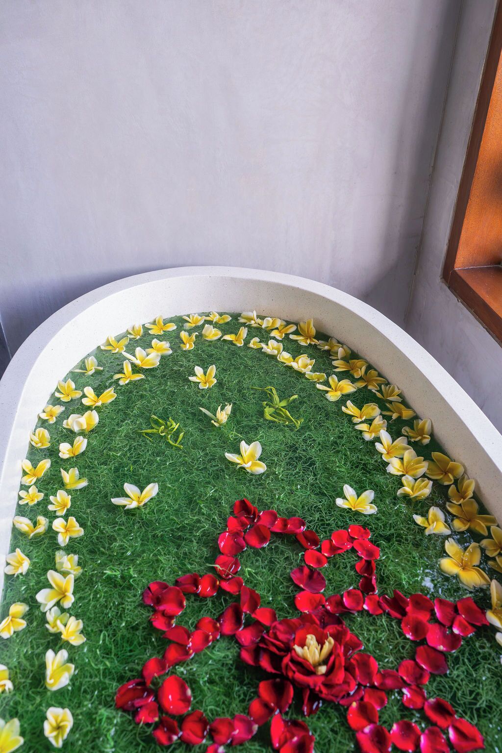 A bathtub with a green grass-like surface and yellow and red flower petals arranged in a pattern.