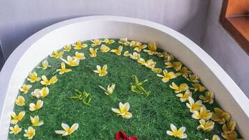 A bathtub with a green grass-like surface and yellow and red flower petals arranged in a pattern.