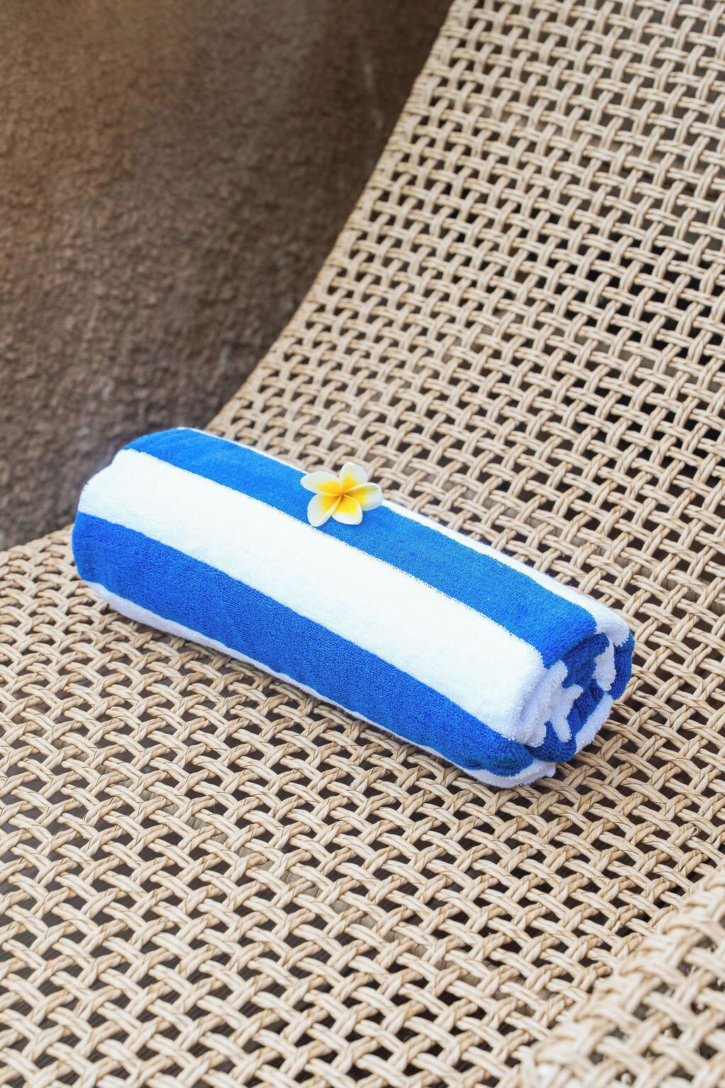 A blue and white striped towel with a yellow flower on a woven chair.