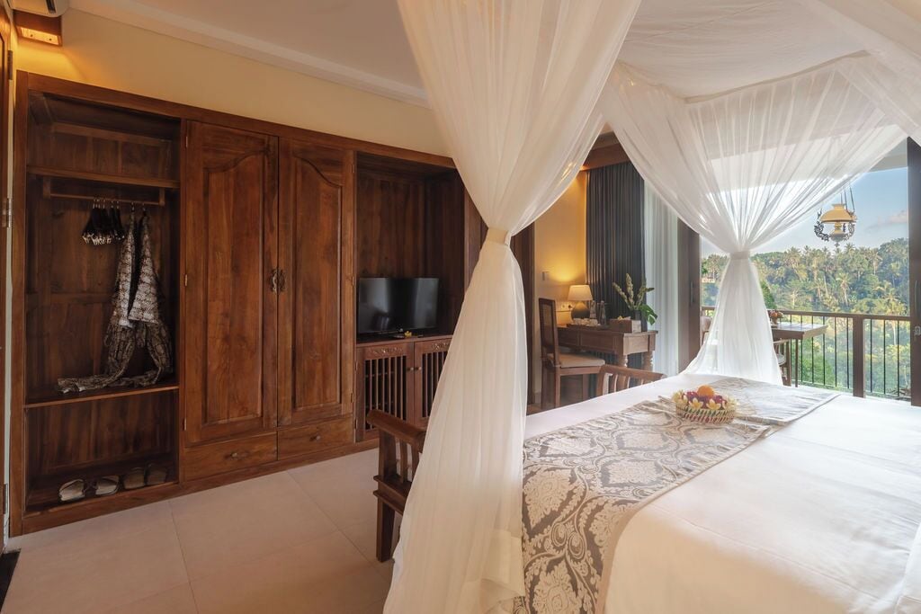 Un dormitorio con una cama grande, un armario de madera, televisión y un balcón con vistas al paisaje.