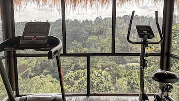 A gym with exercise equipment and a view of a forest through large windows.