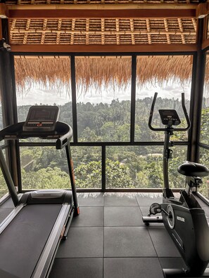 Un gimnasio con equipo de ejercicio y vistas a un bosque a través de amplios ventanales.
