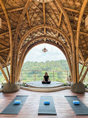 Una persona medita en una habitación con techo de bambú y vista a un paisaje exuberante.