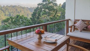 Un balcón de madera con una mesa para dos, un banco acolchado y una vista panorámica de un paisaje boscoso.