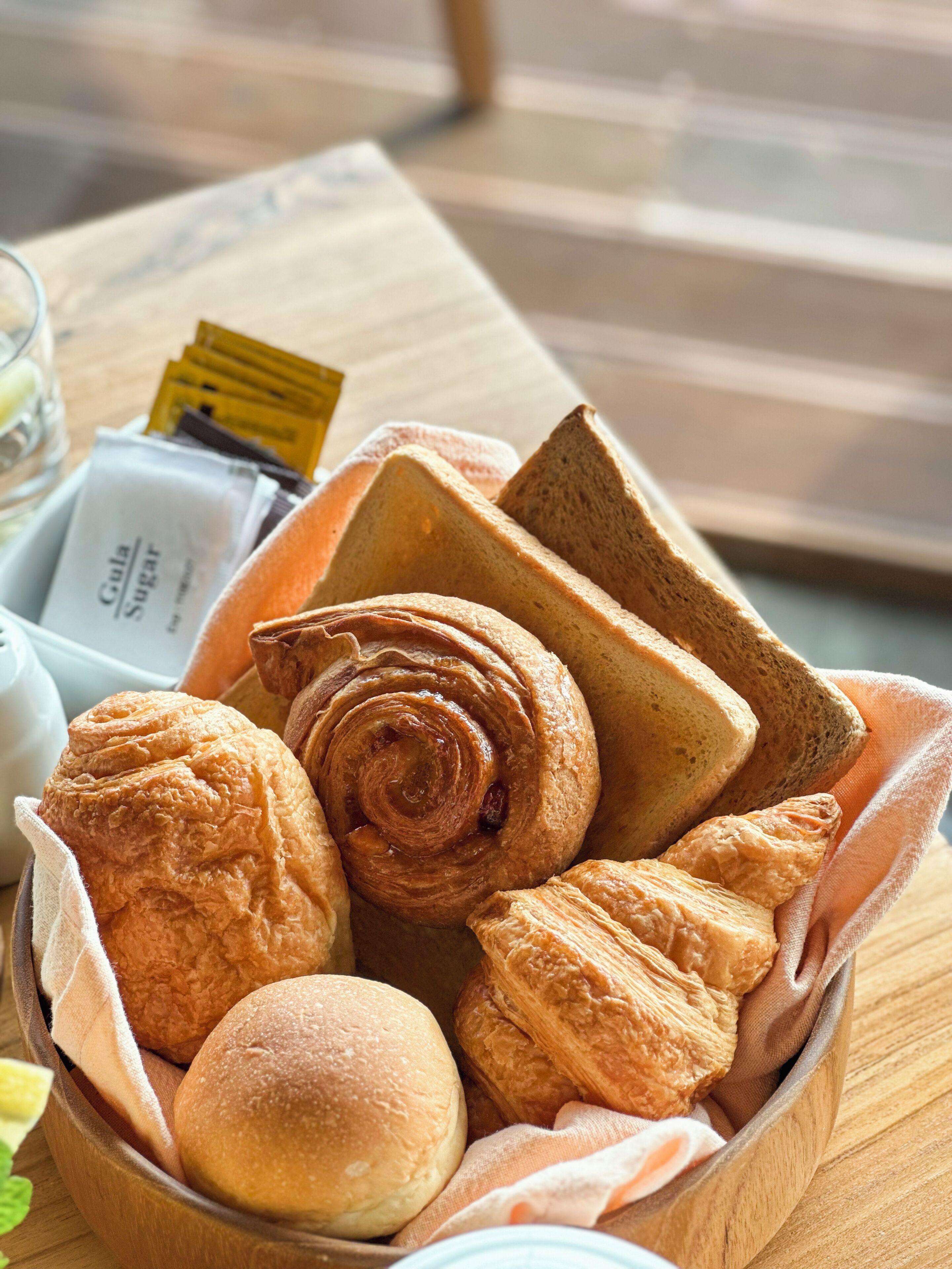 Une table en bois sur laquelle se trouve un panier contenant divers produits de boulangerie, notamment du pain et des pâtisseries.