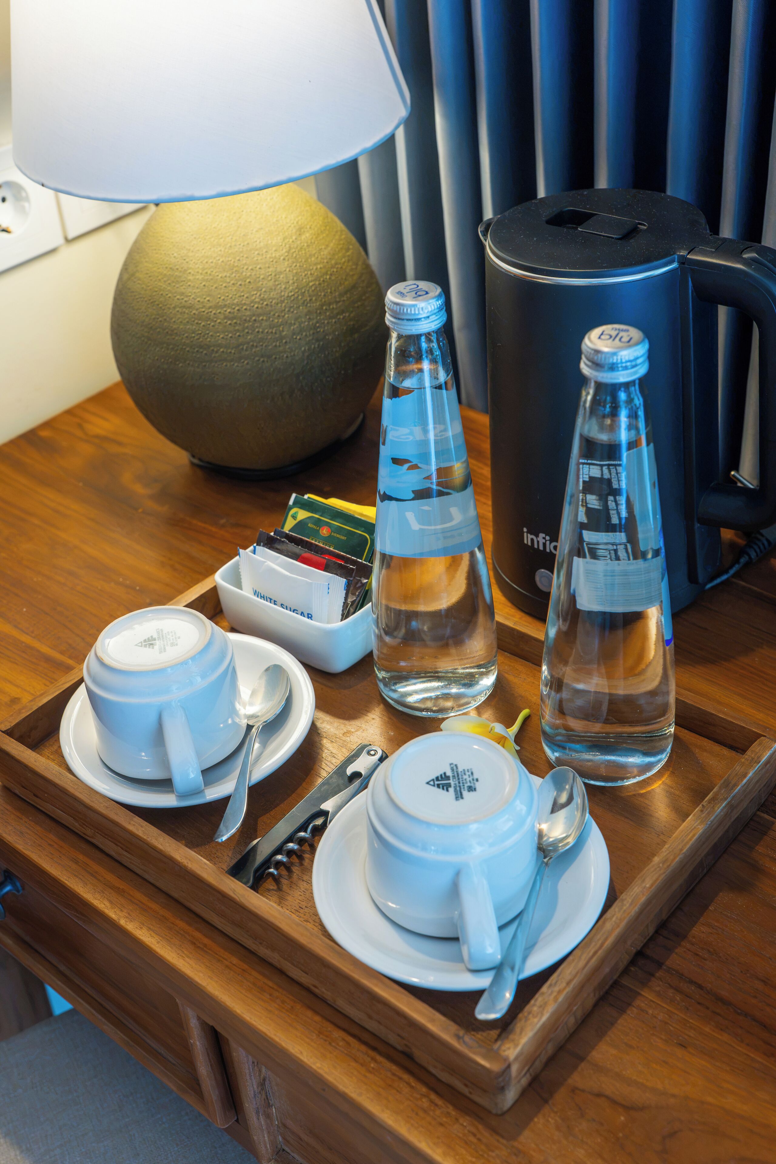 A wooden tray with tea sets, a lamp, a water bottle, and a kettle.