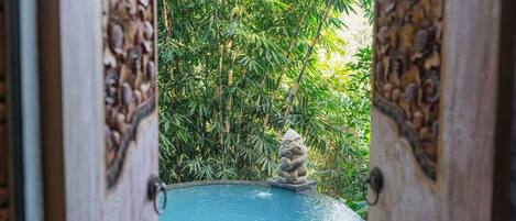 A pool with a stone statue in the center, surrounded by lush greenery.