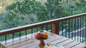 Una mesa de madera con un frutero y un plato en un balcón con vistas a un paisaje boscoso.