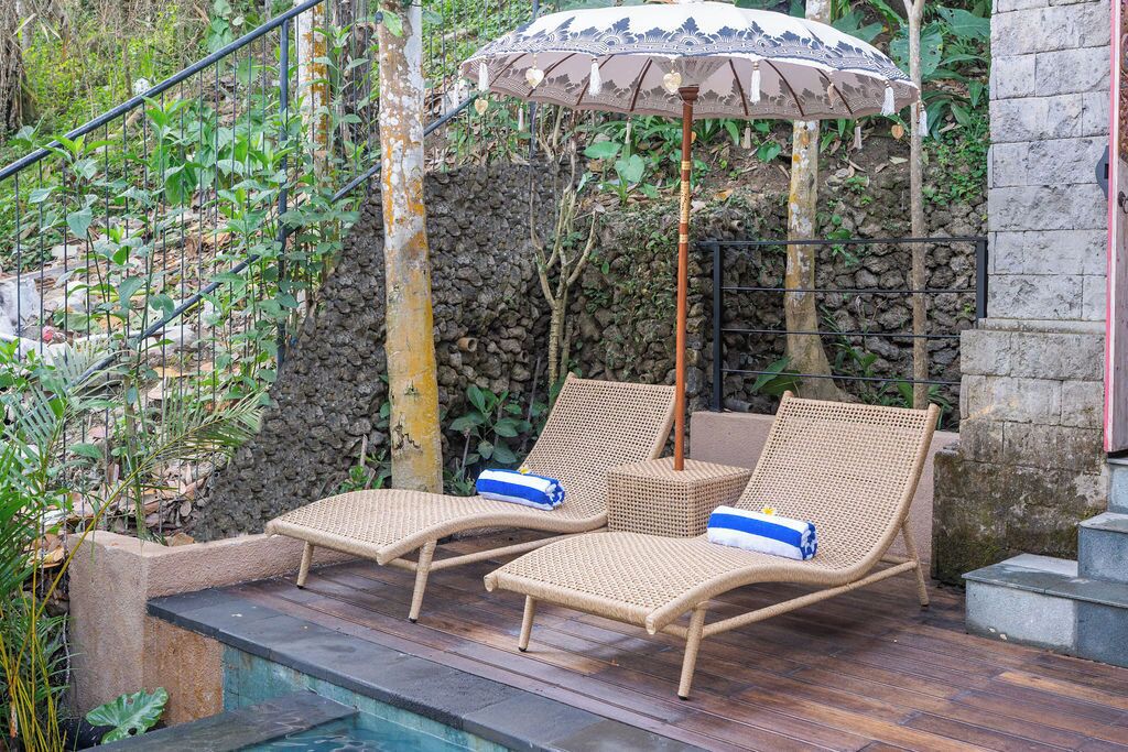 A poolside area with two wicker lounge chairs and a decorative umbrella.