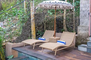 Área de piscina con dos sillones de mimbre y una sombrilla decorativa.