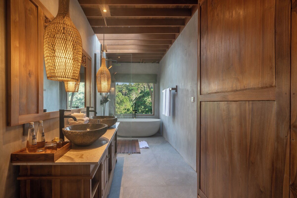 Un baño moderno con una bañera grande, un tocador de madera y un ventanal con vistas al exterior.