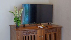 Un mueble de madera con un televisor de pantalla plana encima, un control remoto y una pequeña planta a un lado.