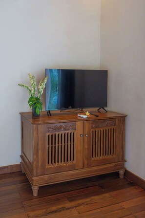 A wooden cabinet with a flat-screen TV on top, a remote control, and a small plant beside it.