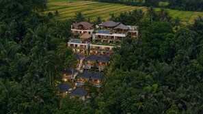 Un resort con varias edificaciones, incluyendo una estructura grande con piscina y algunas construcciones más pequeñas con techos de paja.