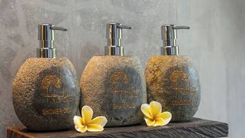 Three stone bottles with pumps, labeled for shower gel, shampoo, and conditioner, on a wooden shelf against a textured wall.