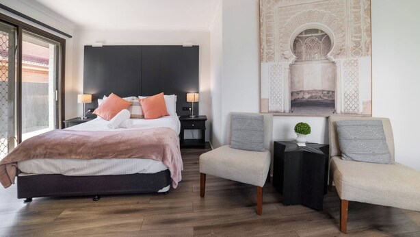 A modern hotel room with a large bed, two bedside tables, a seating area with a chair, and a decorative wall piece. - Room-classic Family Room - Sleeps 4 (Sydney)
