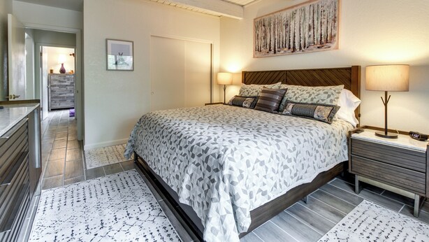 Ein Schlafzimmer mit einem Bett, Nachttischen, einem Bild und einer Tür zu einem anderen Raum.