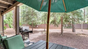 Eine Terrasse im Freien mit Tisch und Stühlen, einem Grill und einem überdachten Bereich mit einem grünen Sonnenschirm.