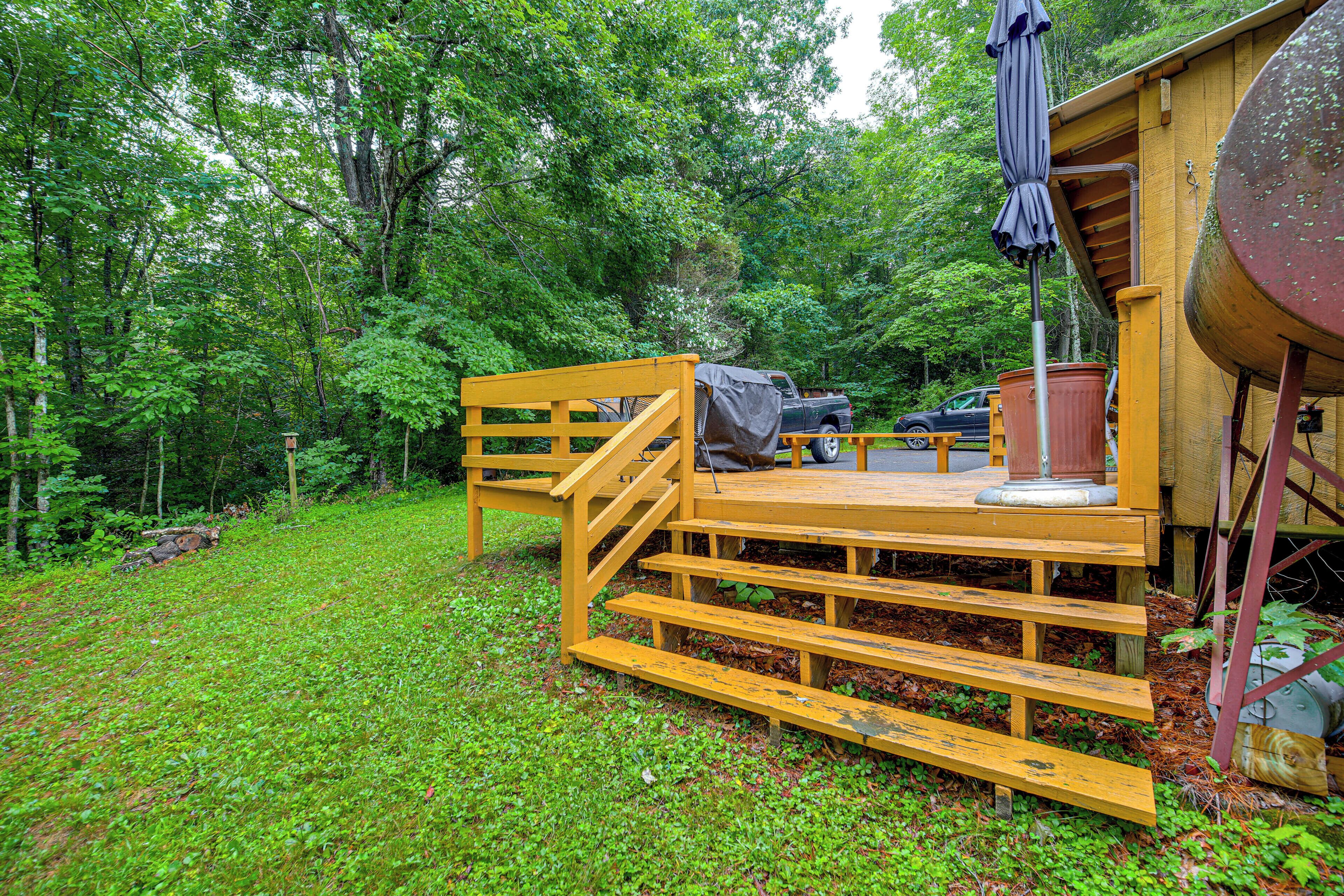 A wooden deck with a staircase leading to a covered area, surrounded by lush greenery.