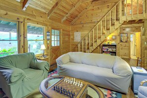 A cozy wooden cabin interior with a sofa, a chess table, and a staircase. - Rustic Cabin w/ Phoenix Mtn Views & Trail Access! (Lansing)