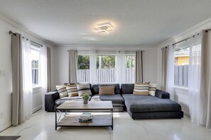 Ein modernes Wohnzimmer mit Ecksofa, Couchtisch und Blick ins Grüne.