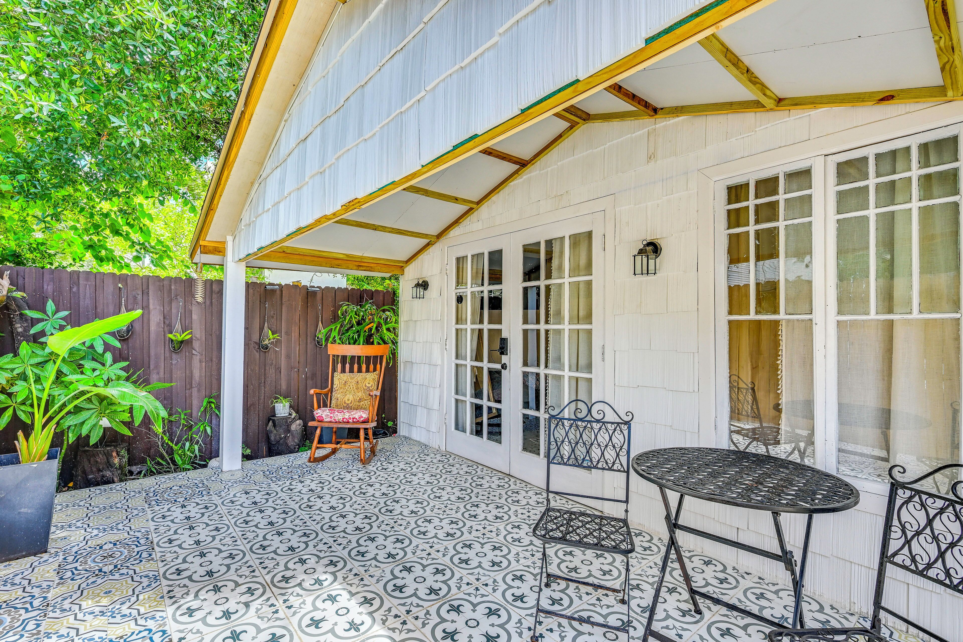 Ein überdachter Patio-Bereich mit gemustertem Bodenbelag, einem Holzstuhl, einem Metalltisch und einem Holenzaun.