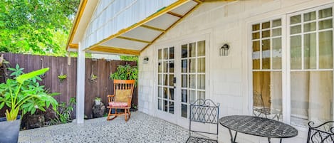 Ein überdachter Patio-Bereich mit gemustertem Bodenbelag, einem Holzstuhl, einem Metalltisch und einem Holenzaun.