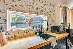 A kitchen with a stone wall, a window with a view, a sink, a microwave, and a cabinet. - Extended Group Getaway 2 Mi to Dtwn & Ybor City! (Tampa)