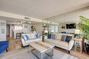A modern living room with a sofa, coffee table, and a large mirror reflecting the space. - Majestic Gulf Views Condo w/ Balcony (Clearwater)