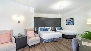 A hotel room with a bed, two bedside tables, a chair, a sofa, and a wall-mounted artwork. - Room-deluxe Family Room - Sleeps 5 (Sydney)