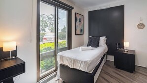 A modern hotel room with a bed, bedside tables, a window with a view, and a wall-mounted artwork. - Room-deluxe Family Room - Sleeps 5 (Sydney)