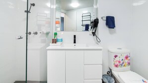 A modern bathroom with a glass shower enclosure, a white sink with a mirror above it, and a toilet with a floral design. - Room-deluxe Family Room - Sleeps 5 (Sydney)