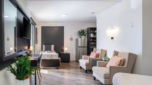 A modern living room with a bed, sofas, a TV, and a kitchen area. - Room-deluxe Family Room - Sleeps 5 (Sydney)