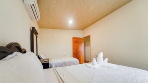 Quarto de hotel com duas camas, teto de madeira e porta que dá para outro aposento.