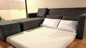 Um sofá modular com um banquinho combinando e uma cama com edredão branco.