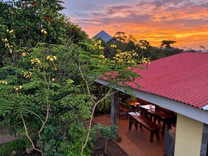 Eine Terrasse mit rotem Dach, umgeben von üppiger Vegetation und blühenden Pflanzen.