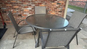 A round metal table with four chairs, set on a concrete patio against a brick wall. - Golf & Chill! Family-Friendly Augusta Home (Augusta)