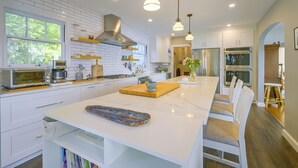 A modern kitchen with white cabinetry, a central island, pendant lighting, and a view of the outdoors through a window. - Charming Waterfront Home with Mt Rainier View (Olympia)