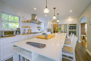 A modern kitchen with white cabinetry, a central island, pendant lighting, and a view of the outdoors through a window. - Charming Waterfront Home with Mt Rainier View (Olympia)