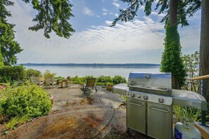A patio with a grill, outdoor seating, and a view of a lake. - Charming Waterfront Home with Mt Rainier View (Olympia)