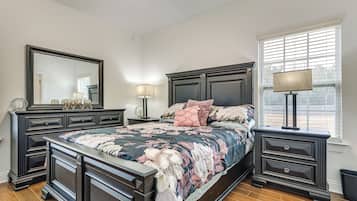 Une chambre à coucher avec un grand lit, une commode, un miroir et une fenêtre avec des stores.