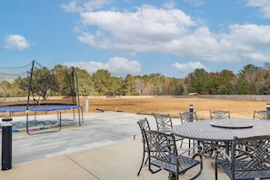 An outdoor patio with a trampoline, metal chairs, and a table. - Screened-In Patio & Trampoline: Creola Getaway! (Creola)