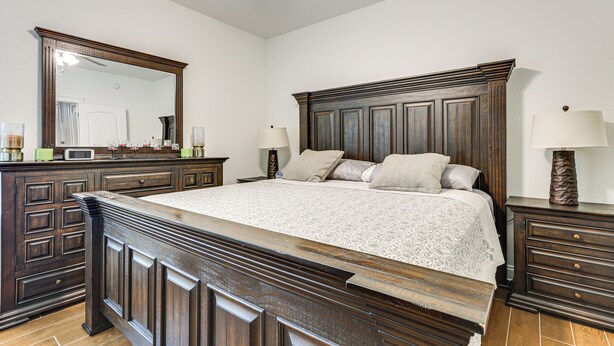 Een slaapkamer met een groot houten bed, een dressoir, een nachtkastje, een spiegel en een plafondventilator.