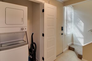 A laundry room with a Whirlpool washer and dryer, a vacuum cleaner, and a door leading to a stairway. - Private Patio, Yard! Townhome Near Pensacola Beach (Gulf Breeze)