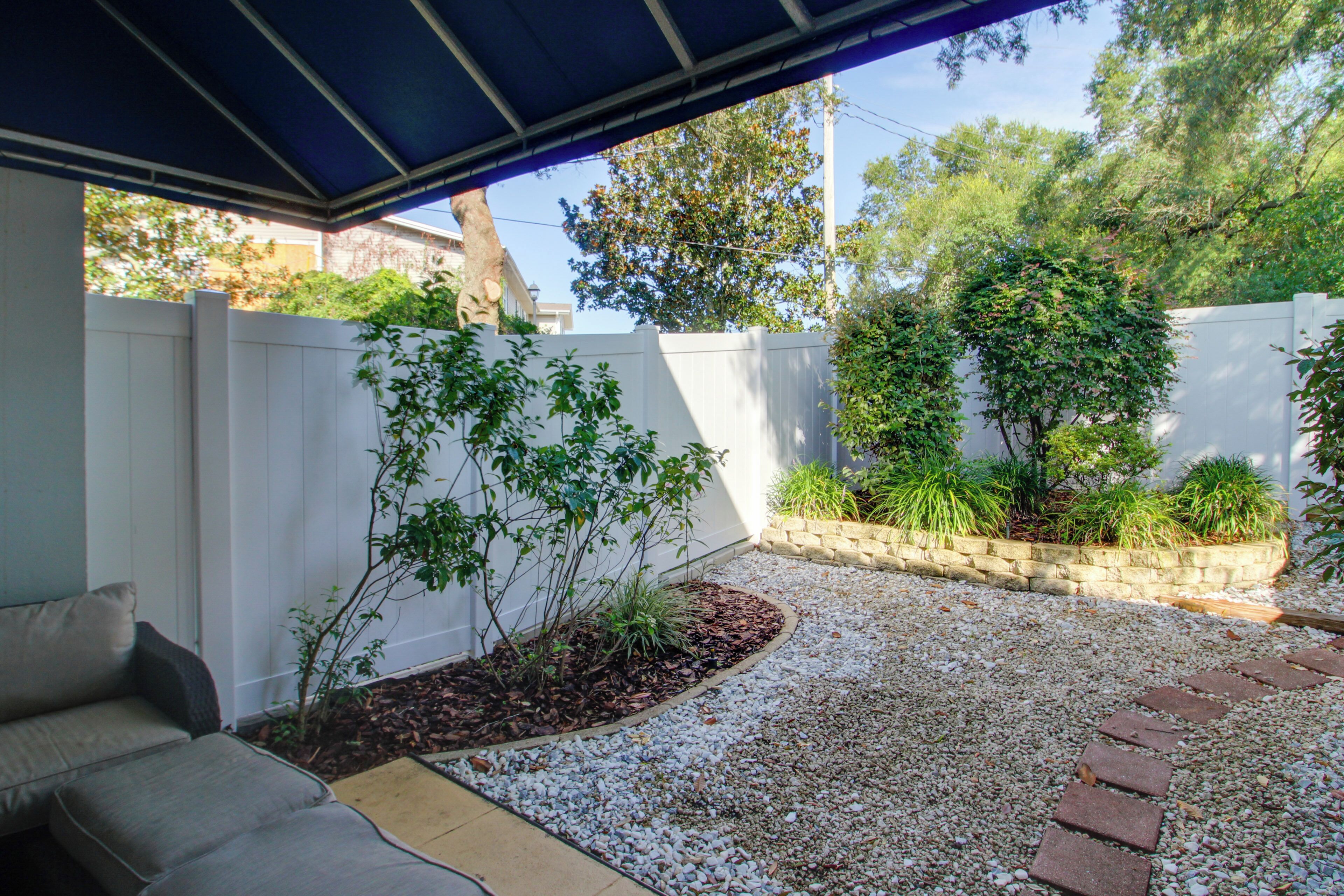 A covered patio area with a white fence, a gravel pathway, and a small garden bed with plants.