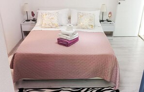 A neatly made bed with a pink bedspread, two white pillows, and a stack of folded towels. - Awesome apartment in Hvar with house sea view (Hvar)