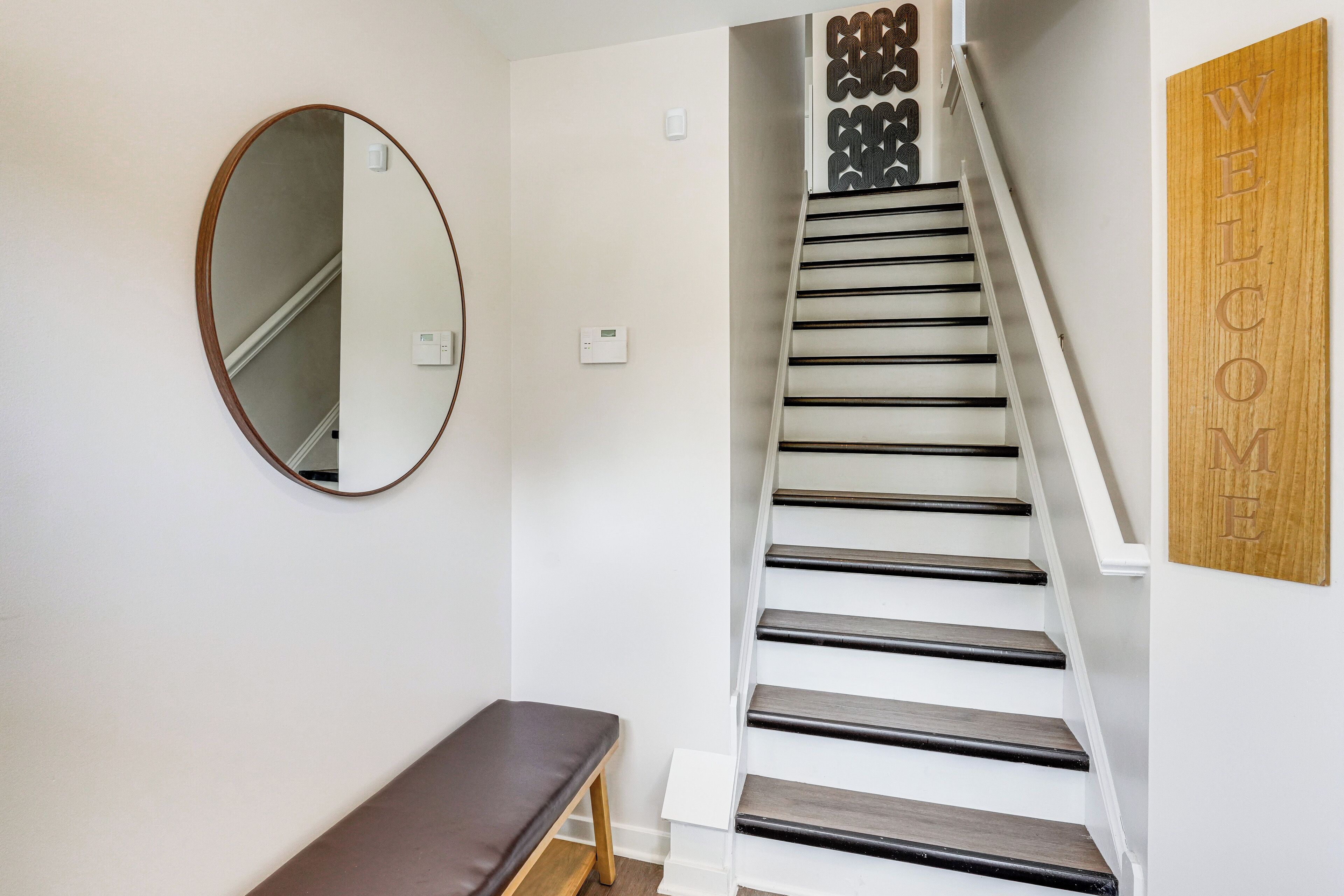 A staircase with a wooden handrail and black steps, a round mirror on the wall, and a bench at the bottom.