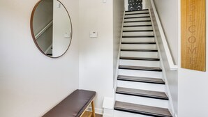 Eine Treppe mit Holzwandhandlauf und schwarzen Stufen, ein runder Spiegel an der Wand und eine Bank am Fußende.