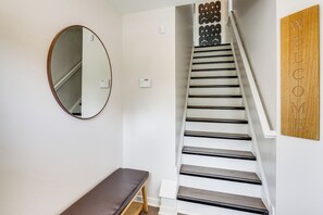 A staircase with a wooden handrail and black steps, a round mirror on the wall, and a bench at the bottom. - Walk to Cleveland Clinic! Contemporary Townhome (Cleveland)