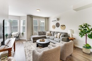 Un salon moderne avec un canapé d’angle, une table basse ronde et un coin repas comprenant une chaise et une table.